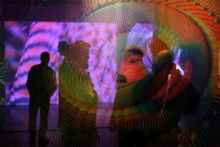 A person standing in front of a very brightly coloured and patterned projected image.