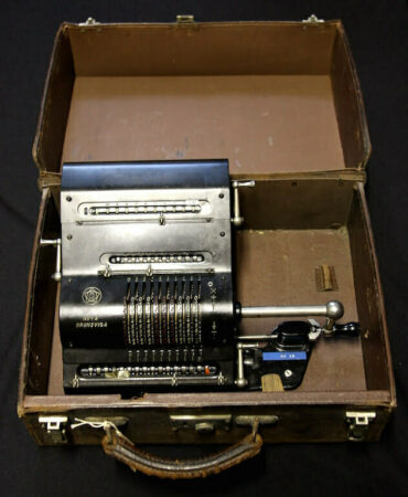 The Brunsviga Nova calculator, which consists of a small metal box containing various dials, switches and levers. This contraption is in a brown leather case.