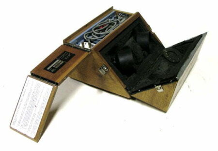 Acoustic Coupler type TC301 (used as early form of modem). A wooden box split into different compartments, with wires in the top compartment and two, black, cup shaped objects in another compartment.