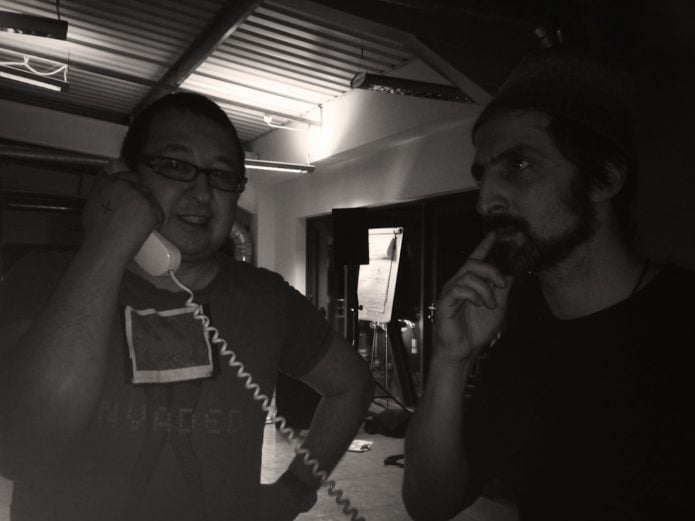 A black and white photograph of NEoN Dj RHL holding an old style telephone while sound artist Tom de Majo looks on ,looking thoughtful.
