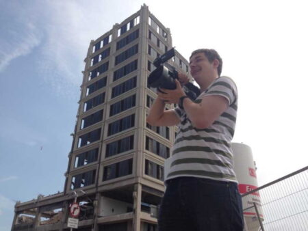 A person with a camera standing by a partially demolished building.