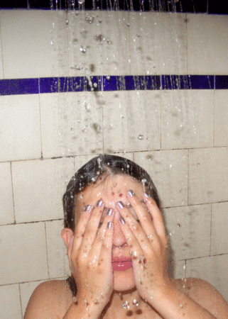 A GIF of a person having a shower in a white tiled shower cubicle. The person looks like they are wiping water from their face.