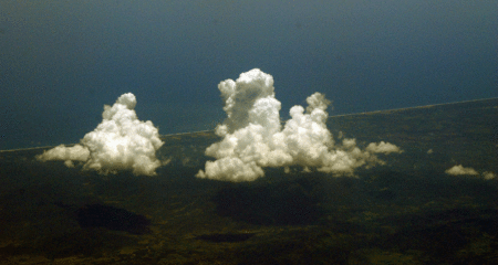 A GIF of an aerial view of white, fluffy clouds moving over a green landscape.