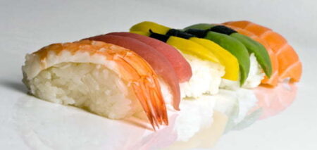 Five pieces of sushi lined up in a row with various toppings, which are, from left to right, prawn, tuna, egg, avocado and salmon.