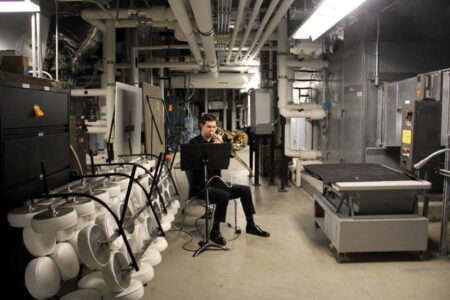 A person playing a trombone in a room full of industrial machinery.
