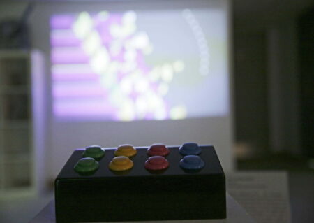 A small black box with eight,games console controller buttons. From left to right the buttons are coloured green,yellow,red and blue.