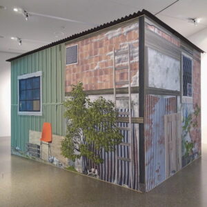 A garden shed or shack inside a white exhibition space.