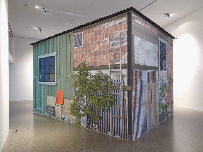 A garden shed or shack inside a white exhibition space.