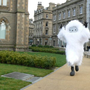 A person in a large white furry costume running round past The McManus Gallery in Dundee.