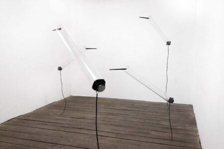 Four strip light tubes suspended in a small white exhibition space.