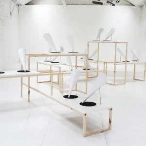 Multiple white conical shapes,each sitting on a black disc, are displayed on large, wooden framed plinths.