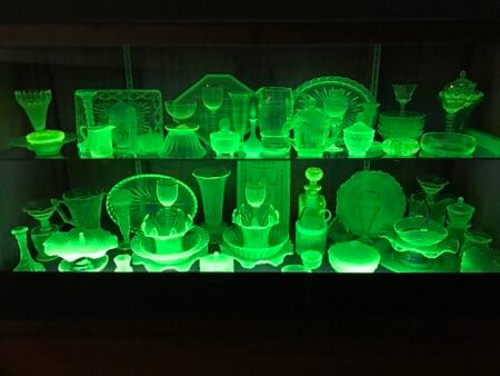 A large collection of glassware exhibited in a glass cabinet. All the glassware is glowing a green colour as if radioactive.