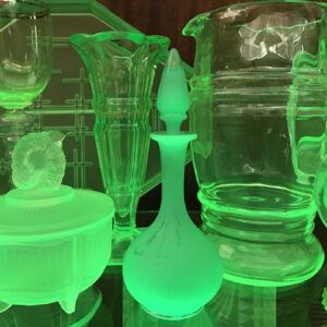 A collection of glassware exhibited in a glass cabinet. All the glassware is glowing a green colour as if radioactive.