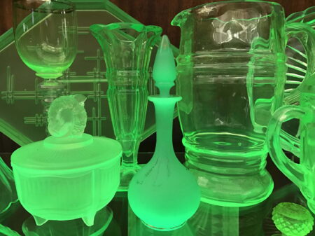 A collection of glassware exhibited in a glass cabinet. All the glassware is glowing a green colour as if radioactive.