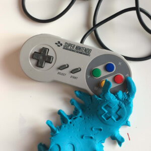 A Super Nintendo games controller next to blue plasticine with indentations of said controller.