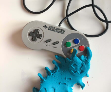A Super Nintendo games controller next to blue plasticine with indentations of said controller.