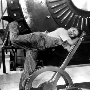 A black and white image of Charlie Chaplin pushing down on a large lever.