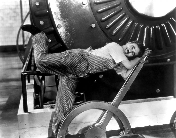 A black and white image of Charlie Chaplin pushing down on a large lever.