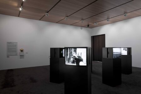 Four black television monitors,each sitting on a black plinth, situated in a white exhibition space.