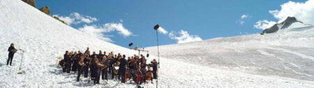 A group of people playing various musical instruments outdoors on a snow covered hill.