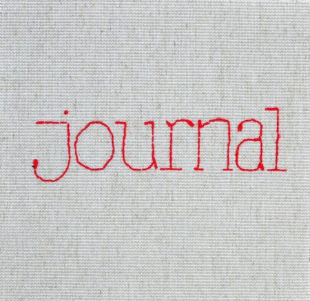 The word "Journal" embroidered with red thread onto plain material.