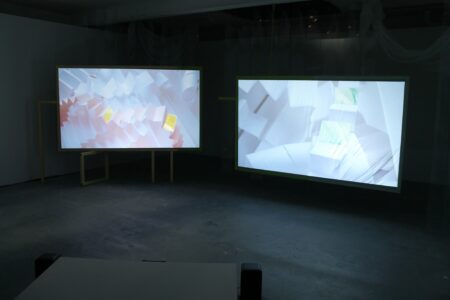 In a dark room sits two screens, both showing images of white,folded paper.