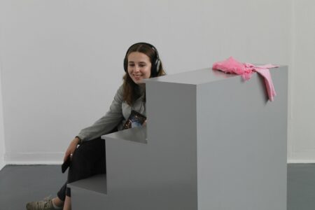 Susie Buchan - Festival Assistant wearing headphones and sitting on a set of grey steps.