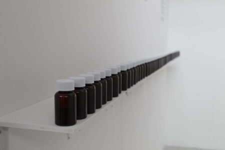 A row of small,brown medicine bottles sit on a white shelf,in a white room.