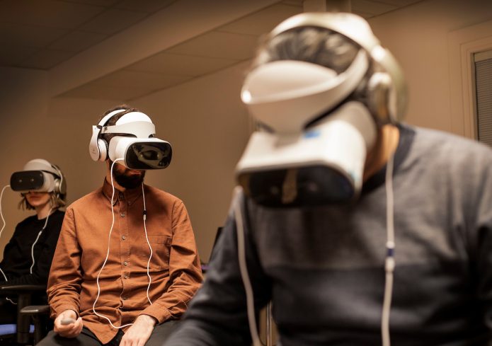 Three people sitting in a room wearing white VR head sets.
