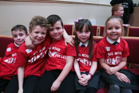 Five school children in red school uniform smiling at the camera.
