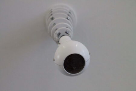 A white security camera in a white room, hanging from the ceiling.