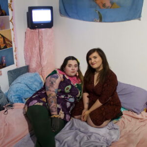 Two people lounging on multi coloured cushions with a portable television in the back ground.