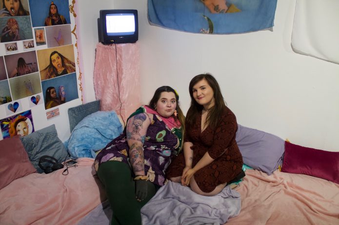 Two people lounging on multi coloured cushions with a portable television in the back ground.