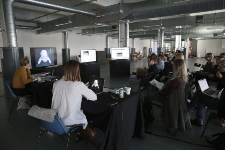 Group of people in a large office space in the Vision Building,Dundee, watching a white computer generated image of a person on a large monitor.