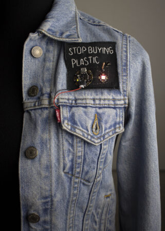 A blue denim jacket with a Stop Buying Plastic patch sewn on.