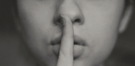 A black and white image of a close up of a persons face, holding a finger against their lips.