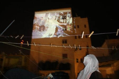 Person staring up at a blurred image that has been projected on to a white building.
