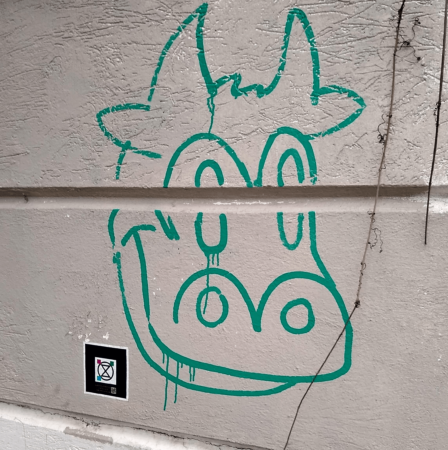 Green line drawing of a cartoon like cows head on a white wall.