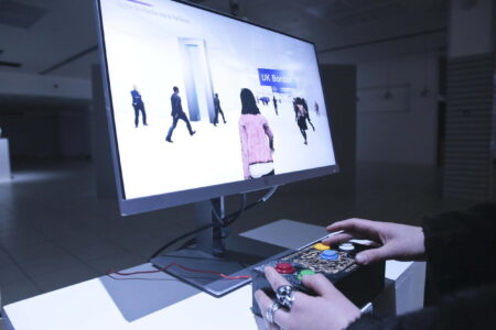 A persons hands on a games controller playing a game on a computer monitor.