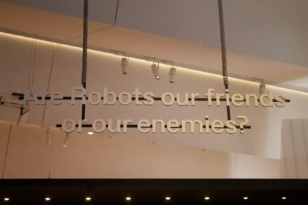 The words " Are Robots our friends or our enemies?", suspended in the air, in a white room.