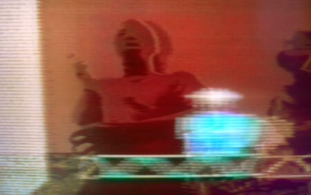 A blurred image of a person dancing. This image is coloured red. Superimposed over this image is what looks like a blurry/ glitchy image of a whiskey decanter coloured bright blue, which is sitting on a computer generated image of steel girder, which is green in colour.
