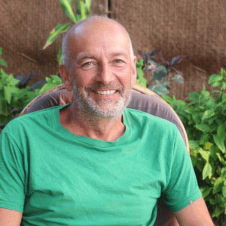 The artist George Barber sitting on a chair and smiling at the camera. He is wearing a green tee shirt.