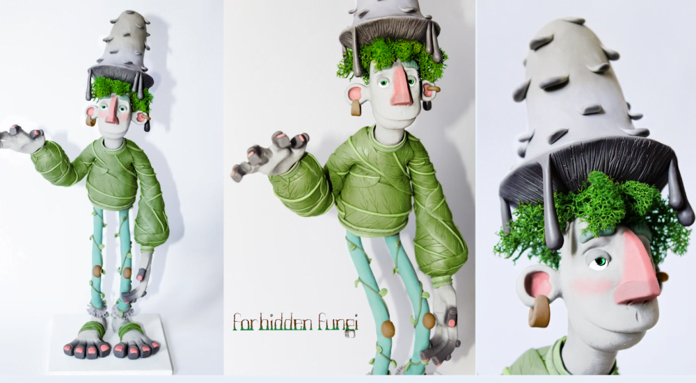 Character Maquette of Prin, half-fungi half-man his hair is green moss, his hat a grey mushroom, his clothes leaves and vines. He has a long, slightly goofy face and is waving with his right hand.