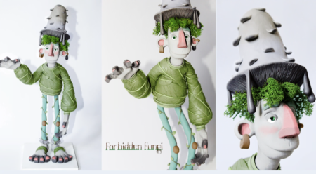 Half-fungi, half-man his hair is green moss, his hat a grey mushroom, his clothes made from green leaves and vines. He has a long, slightly goofy face and is waving with his right hand.