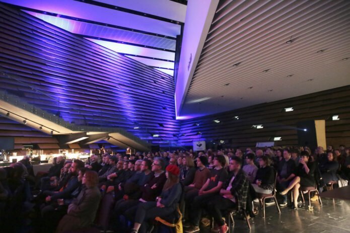 A large group of people,inside the V&A Dundee, watching Bladerunner at NEoN Digital Arts Festival 2019.