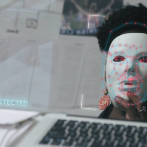 Person with plain white mask staring at a computer screen. Superimposed on the mask are red dots connected by blue lines.