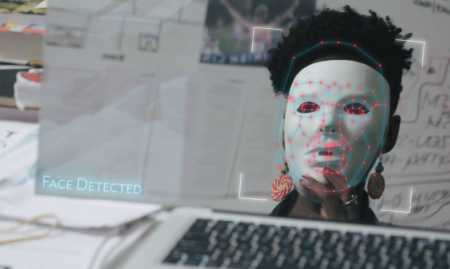 Person with plain white mask staring at a computer screen. Superimposed on the mask are red dots connected by blue lines.
