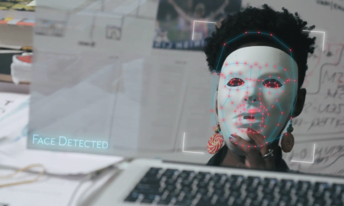Person with plain white mask staring at a computer screen.