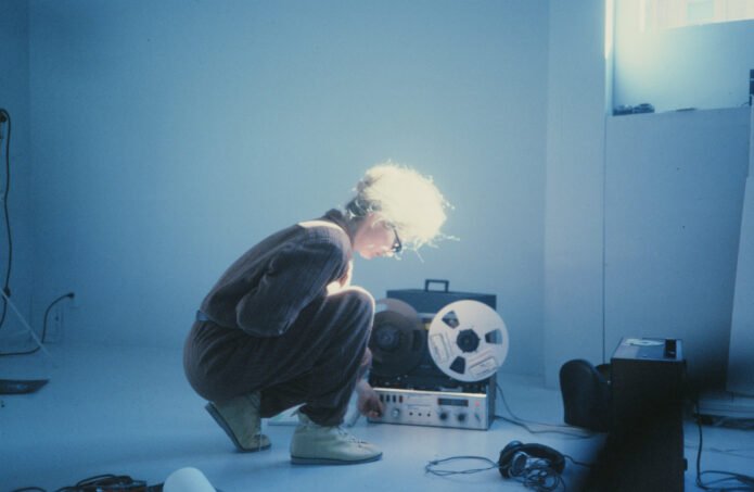 person in a white room using a reel to reel tape machine.