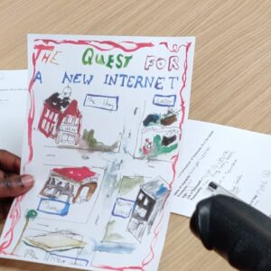 a young person sitting at a desk, holding a piece of paper with four illustrations on it. The heading on the paper reads " The quest for a new internet."